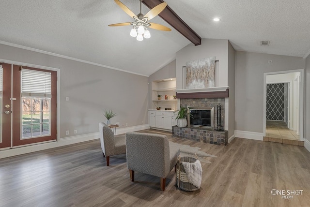 living room with ceiling fan, lofted ceiling with beams, wood-type flooring, a textured ceiling, and a fireplace