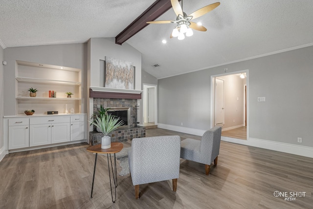 living room with vaulted ceiling with beams, ceiling fan, a textured ceiling, a fireplace, and wood-type flooring