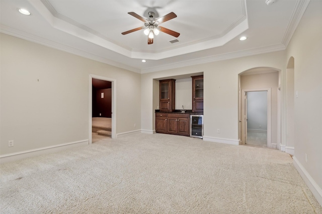 unfurnished living room with light carpet, a raised ceiling, crown molding, ceiling fan, and beverage cooler