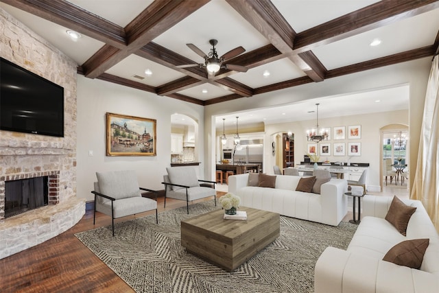 living room with coffered ceiling, ceiling fan with notable chandelier, a fireplace, beam ceiling, and wood-type flooring