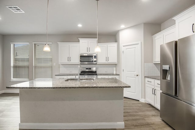 kitchen with white cabinetry, sink, stainless steel appliances, decorative light fixtures, and a center island with sink