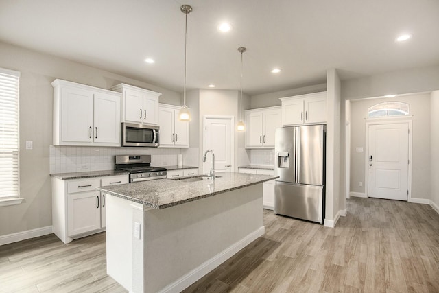 kitchen with dark stone counters, stainless steel appliances, sink, white cabinetry, and an island with sink