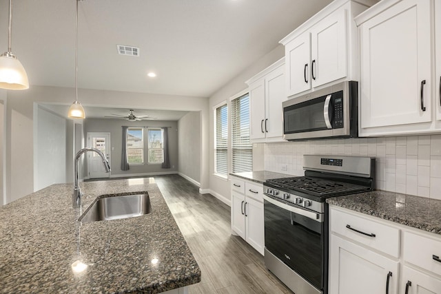 kitchen with appliances with stainless steel finishes, light wood-type flooring, sink, white cabinetry, and hanging light fixtures