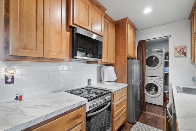 kitchen featuring sink, stacked washer and dryer, dark hardwood / wood-style floors, tasteful backsplash, and stainless steel appliances