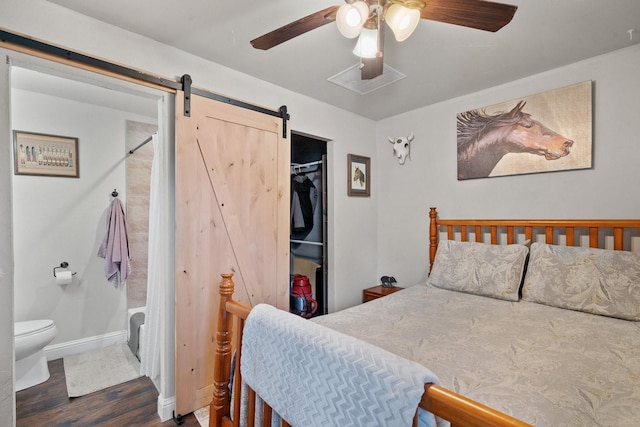 bedroom featuring ceiling fan, dark wood-type flooring, a barn door, connected bathroom, and a closet