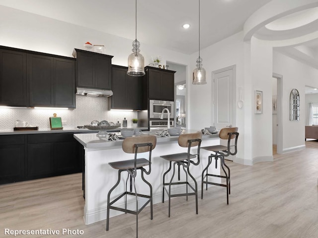 kitchen featuring a kitchen breakfast bar, a center island with sink, decorative light fixtures, and light hardwood / wood-style flooring