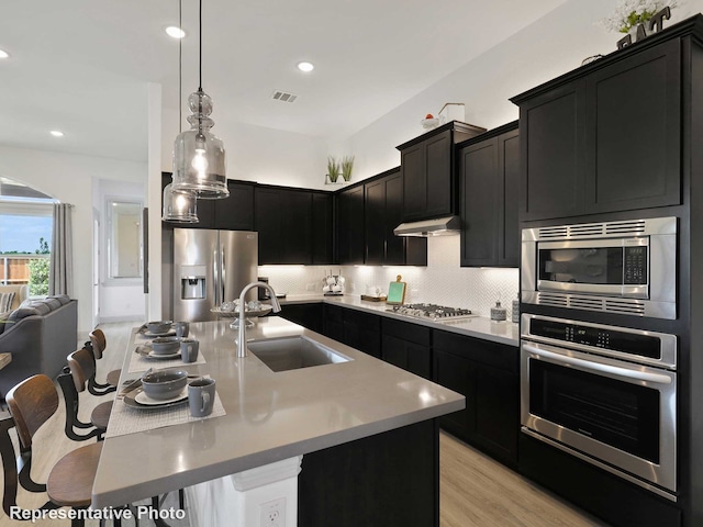 kitchen featuring a kitchen island with sink, sink, light hardwood / wood-style flooring, appliances with stainless steel finishes, and a breakfast bar area