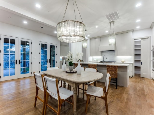 dining room featuring a chandelier, french doors, light hardwood / wood-style flooring, and sink