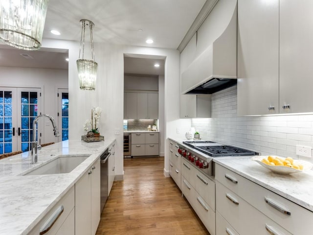 kitchen featuring appliances with stainless steel finishes, light wood-type flooring, beverage cooler, sink, and hanging light fixtures