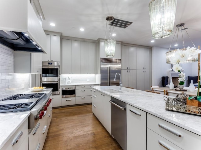 kitchen with appliances with stainless steel finishes, custom exhaust hood, sink, decorative light fixtures, and light hardwood / wood-style floors