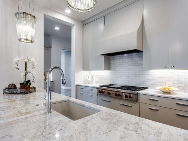 kitchen with light stone countertops, custom range hood, sink, an inviting chandelier, and stainless steel gas stovetop