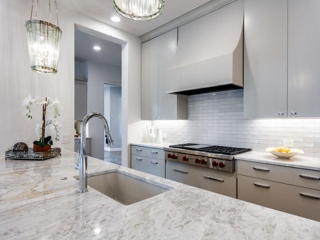 kitchen featuring sink, wall chimney range hood, backsplash, light stone countertops, and stainless steel gas cooktop