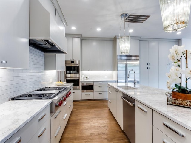 kitchen with appliances with stainless steel finishes, custom range hood, decorative light fixtures, light hardwood / wood-style floors, and white cabinetry