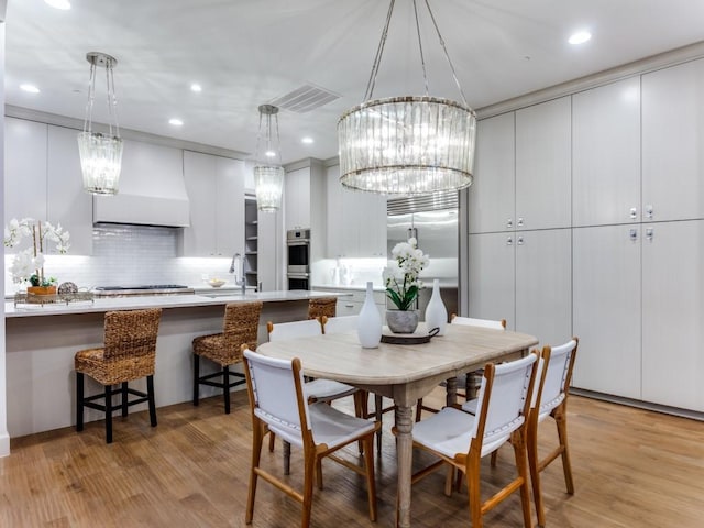 dining area with a notable chandelier, light wood-type flooring, and sink