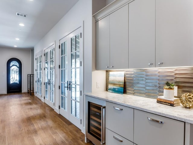 bar with light stone countertops, french doors, tasteful backsplash, beverage cooler, and light hardwood / wood-style flooring