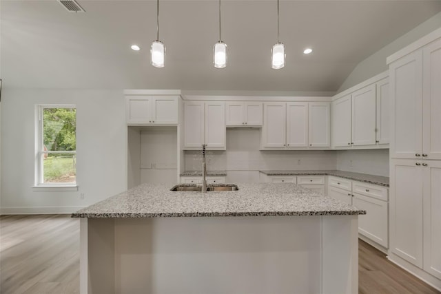 kitchen featuring light stone counters, vaulted ceiling, light hardwood / wood-style floors, white cabinetry, and an island with sink