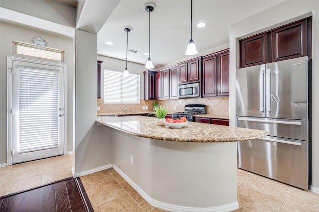 kitchen featuring appliances with stainless steel finishes, tasteful backsplash, hanging light fixtures, light stone counters, and kitchen peninsula