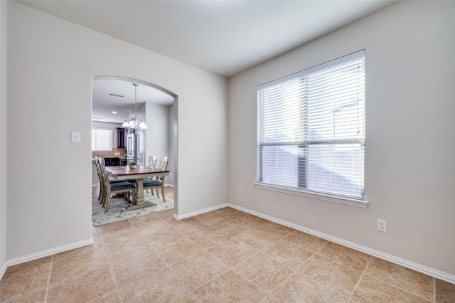 tiled spare room featuring a wealth of natural light and a notable chandelier