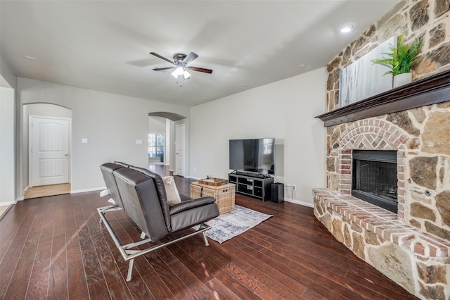 living room featuring a stone fireplace, ceiling fan, and dark hardwood / wood-style floors