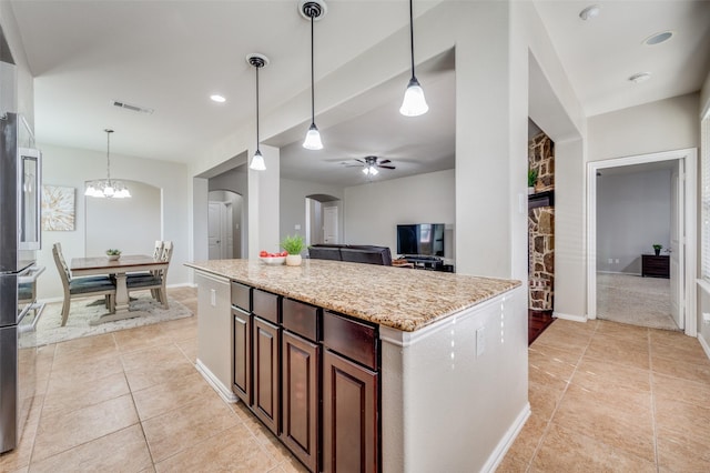 kitchen with light tile patterned flooring, a center island, light stone counters, and decorative light fixtures