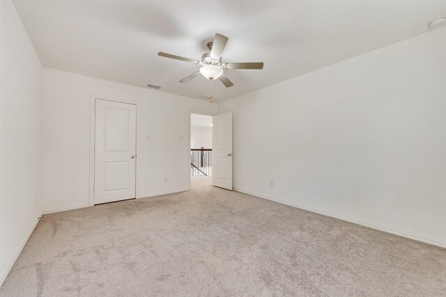 empty room featuring ceiling fan, visible vents, baseboards, and light colored carpet