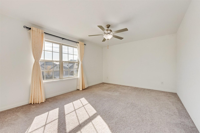 spare room featuring light carpet, ceiling fan, and baseboards