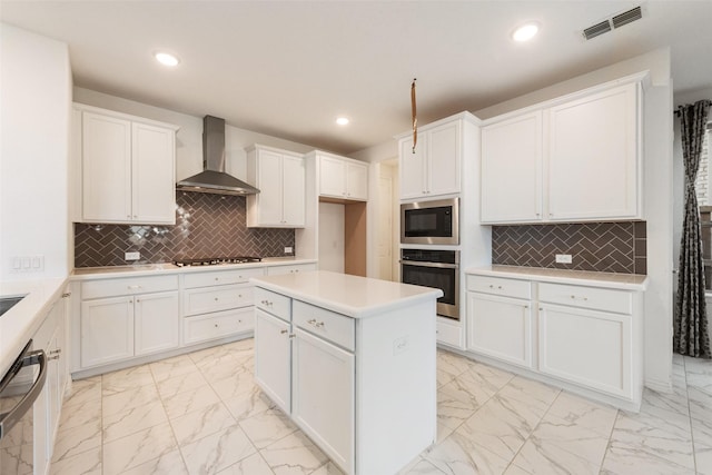 kitchen featuring marble finish floor, stainless steel appliances, light countertops, white cabinetry, and wall chimney exhaust hood