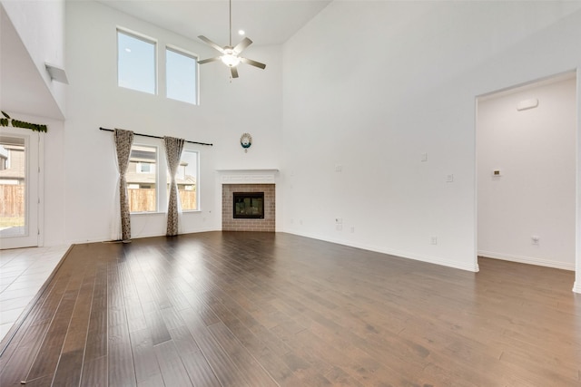 unfurnished living room with a high ceiling, wood finished floors, a ceiling fan, baseboards, and a brick fireplace