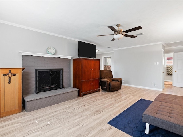 living room featuring ceiling fan, ornamental molding, a brick fireplace, and light hardwood / wood-style flooring