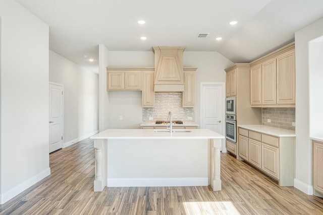 kitchen with a center island with sink, built in microwave, oven, light hardwood / wood-style flooring, and backsplash