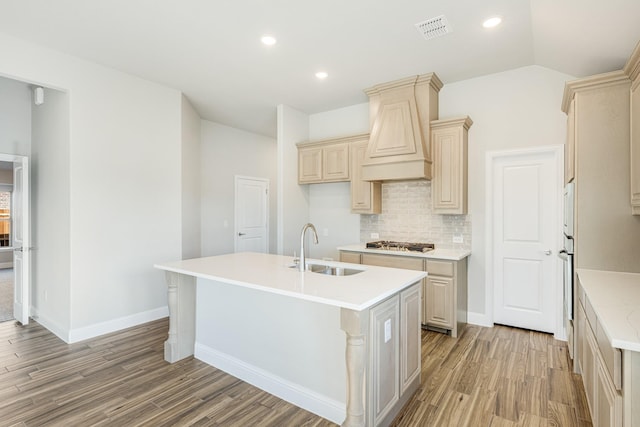 kitchen with sink, vaulted ceiling, custom range hood, stainless steel gas stovetop, and a center island with sink