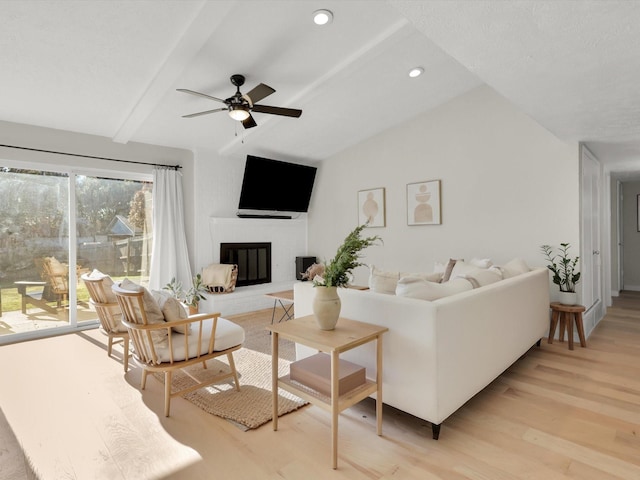 living room with a fireplace, lofted ceiling with beams, light hardwood / wood-style floors, and ceiling fan