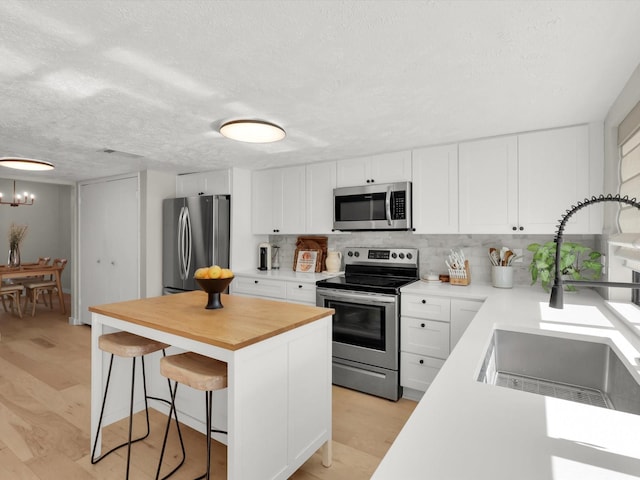 kitchen with sink, light hardwood / wood-style flooring, a breakfast bar, stainless steel appliances, and white cabinets