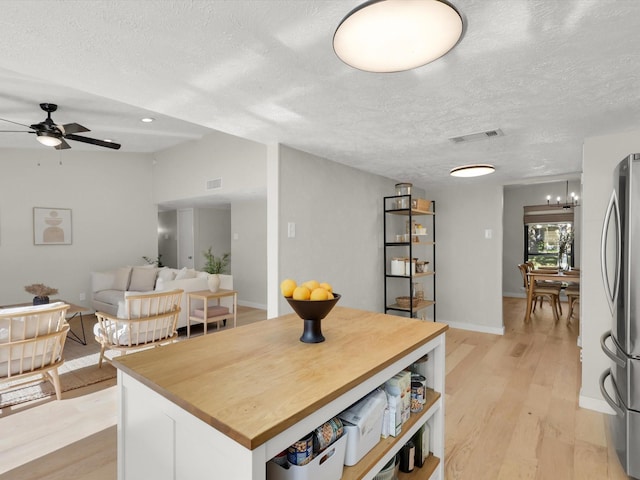 kitchen with a textured ceiling, stainless steel refrigerator, a kitchen island, light hardwood / wood-style floors, and white cabinets