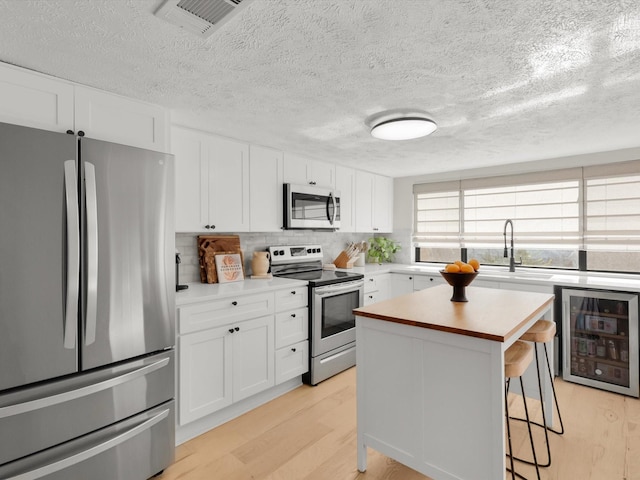 kitchen featuring a breakfast bar area, white cabinetry, stainless steel appliances, a center island, and light hardwood / wood-style floors