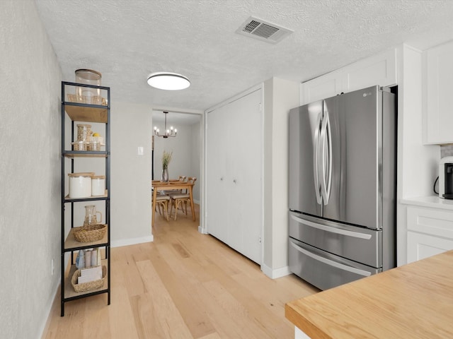 kitchen featuring a chandelier, light hardwood / wood-style flooring, stainless steel fridge, pendant lighting, and white cabinets