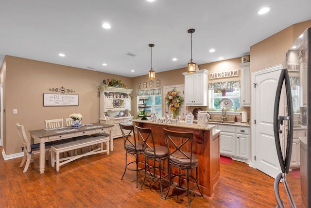 kitchen featuring black refrigerator, decorative light fixtures, white cabinetry, dark hardwood / wood-style flooring, and a center island