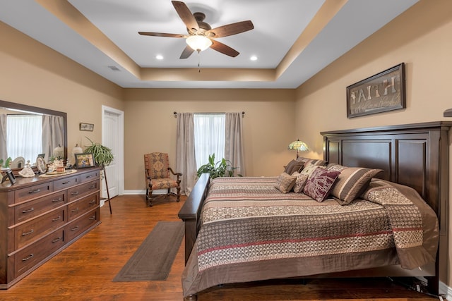 bedroom featuring dark wood-type flooring, ceiling fan, a raised ceiling, and multiple windows