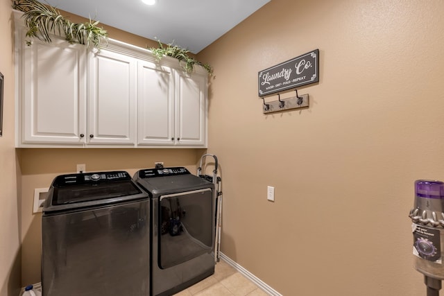 clothes washing area with washing machine and clothes dryer, light tile patterned floors, and cabinets