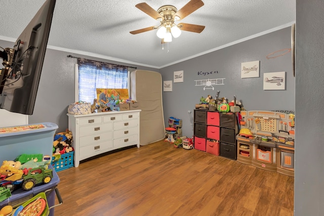 recreation room featuring hardwood / wood-style flooring, ceiling fan, ornamental molding, and a textured ceiling