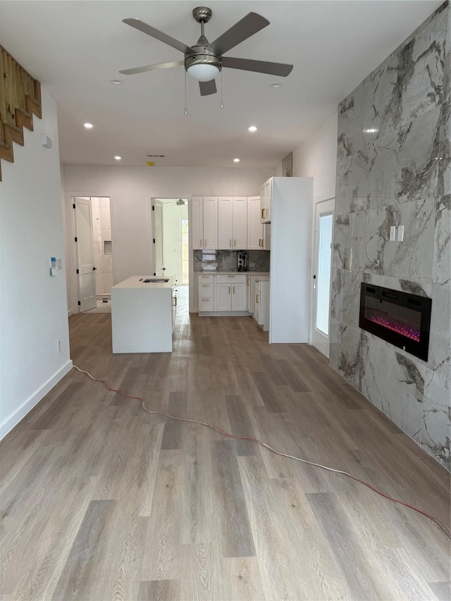 unfurnished living room with sink, light hardwood / wood-style flooring, ceiling fan, a fireplace, and heating unit