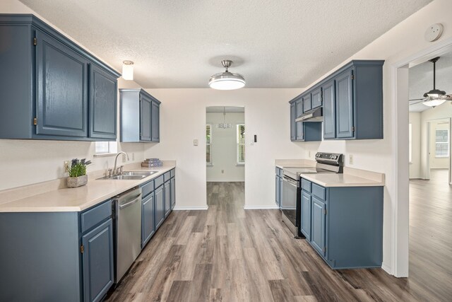 kitchen featuring appliances with stainless steel finishes, dark hardwood / wood-style flooring, sink, blue cabinetry, and hanging light fixtures