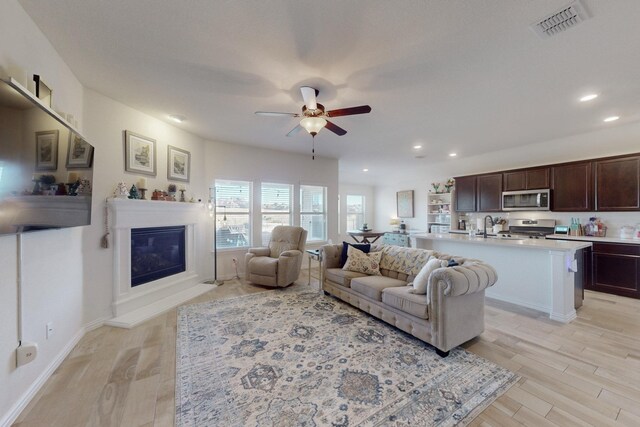 living room featuring light wood-type flooring, ceiling fan, and sink