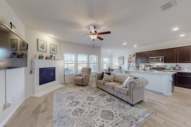 living room with ceiling fan, sink, and light hardwood / wood-style flooring