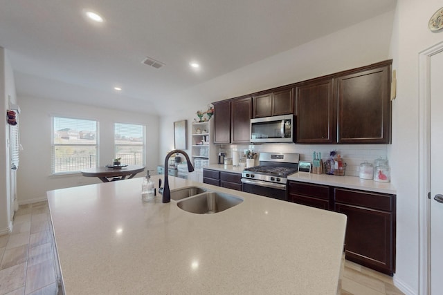 kitchen with sink, backsplash, stainless steel appliances, and an island with sink