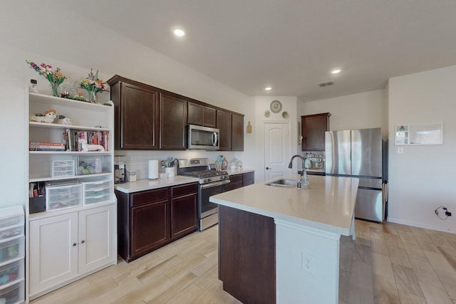 kitchen featuring sink, dark brown cabinets, light wood-type flooring, appliances with stainless steel finishes, and a kitchen island with sink