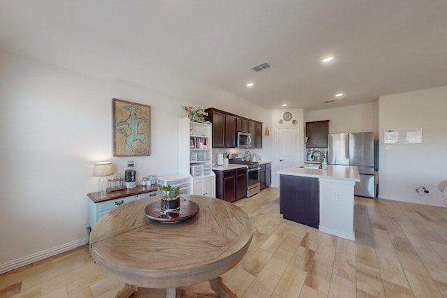 kitchen with sink, dark brown cabinets, stainless steel appliances, light hardwood / wood-style floors, and a center island with sink