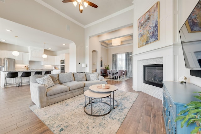 living room featuring a tiled fireplace, ceiling fan, crown molding, and dark wood-type flooring