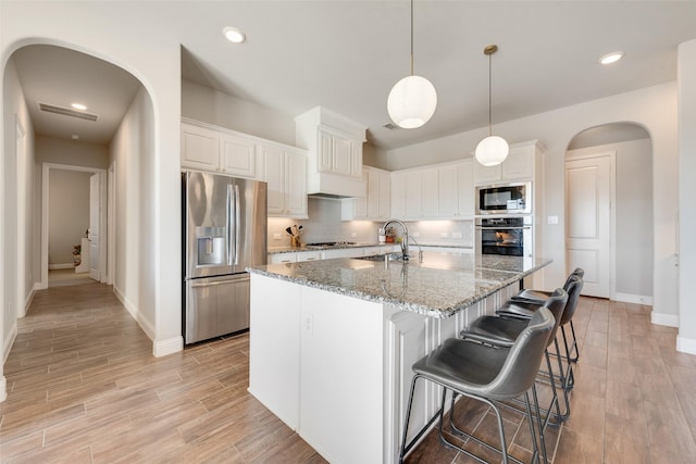 kitchen with appliances with stainless steel finishes, sink, stone counters, white cabinetry, and an island with sink