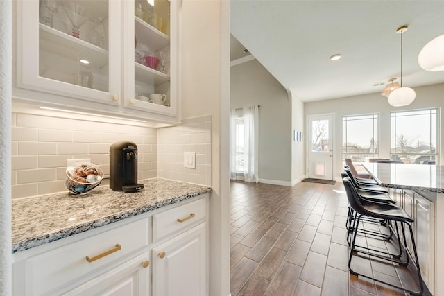 kitchen featuring decorative backsplash, white cabinetry, hanging light fixtures, and light stone counters